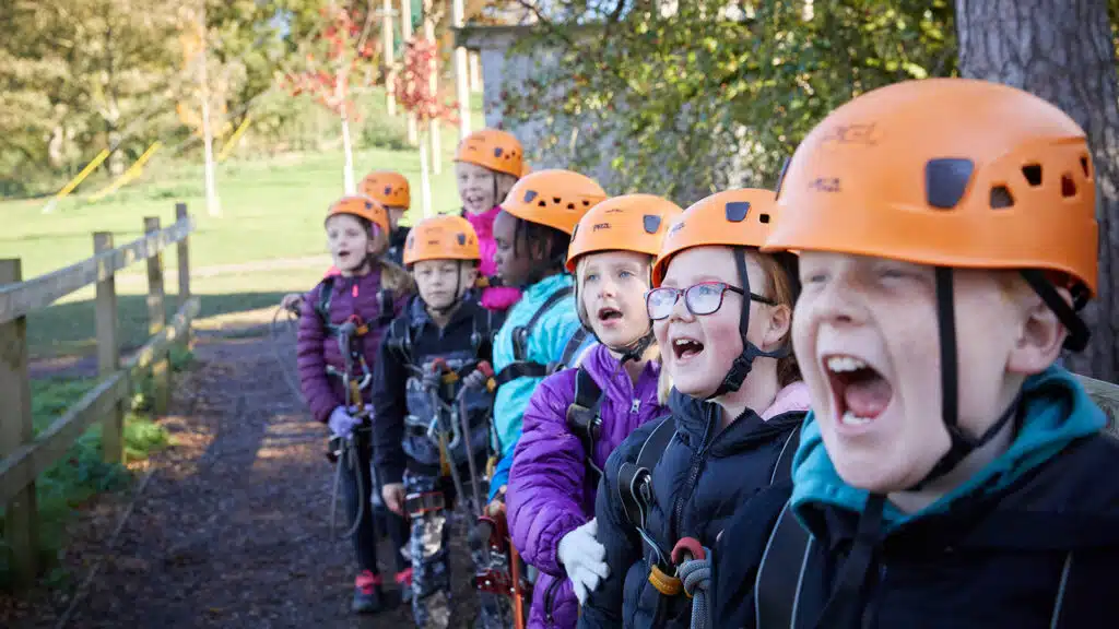 A group of excited children wearing helmets and outdoor gear in a park, with one boy shouting enthusiastically.