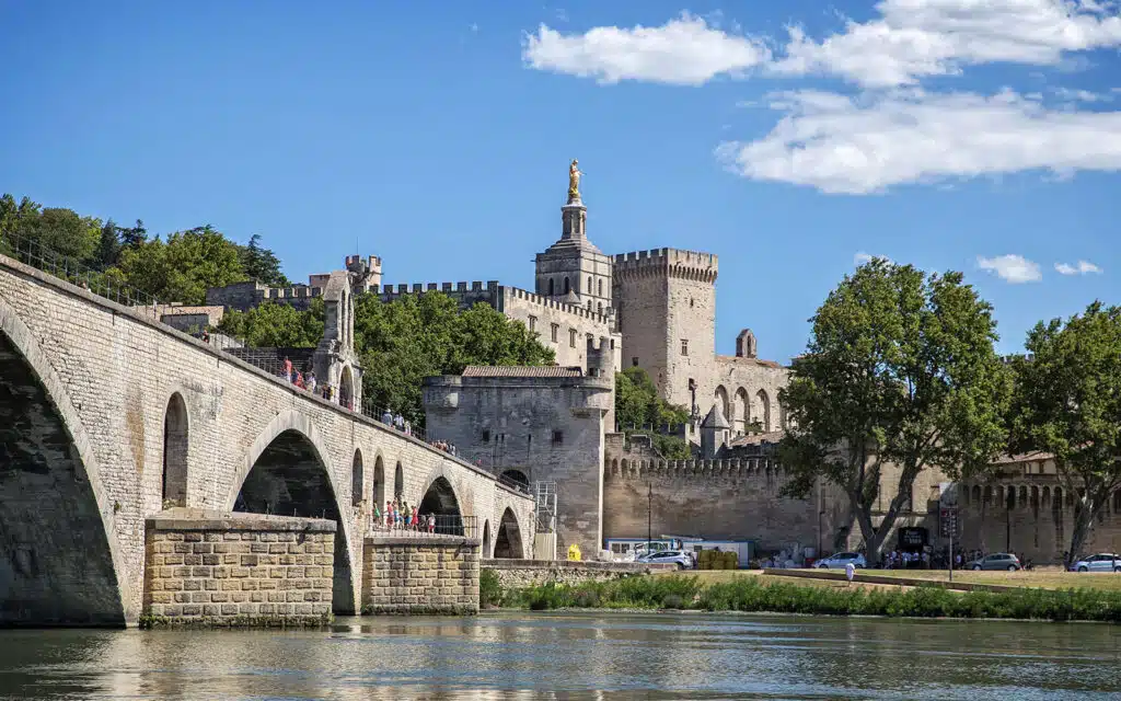 Historic stone bridge with arches leading to an ancient fortified tower under a clear blue sky, perfect for multi-activity outings.