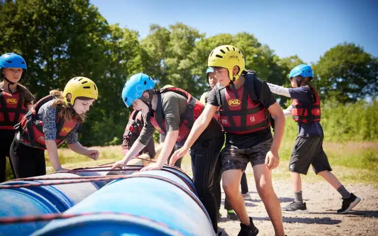 Group of teenagers wearing safety gear engaged in a multi-activity day, building a raft together on a sunny day.