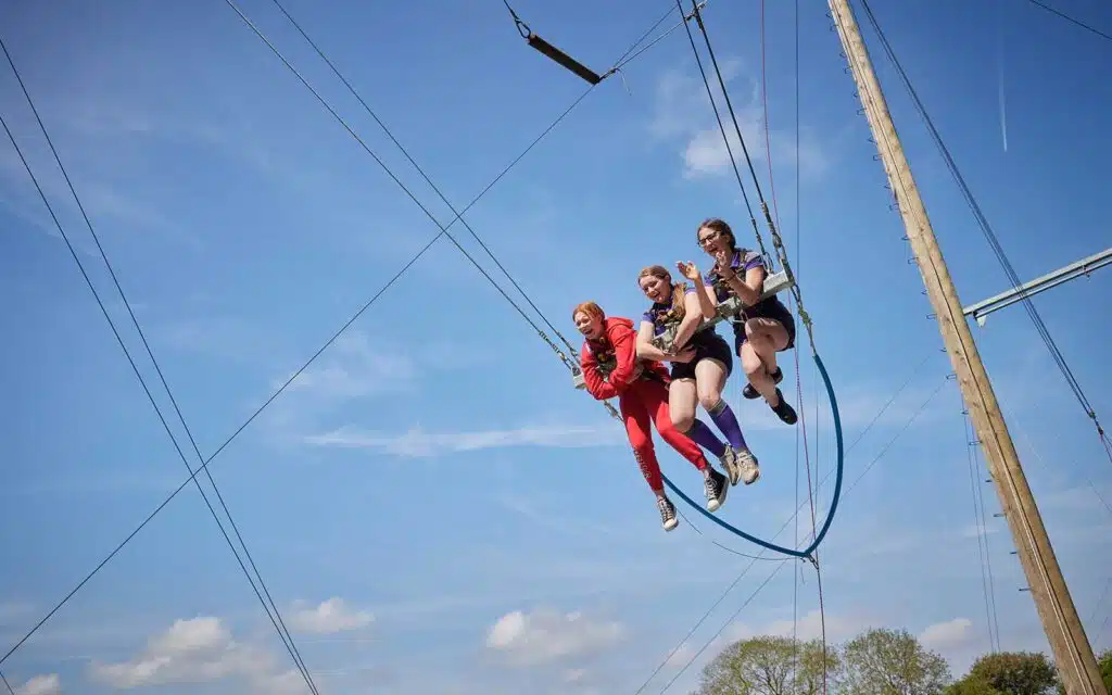 Three people riding a zip line against a clear blue sky, enjoying the thrill of the adventure.