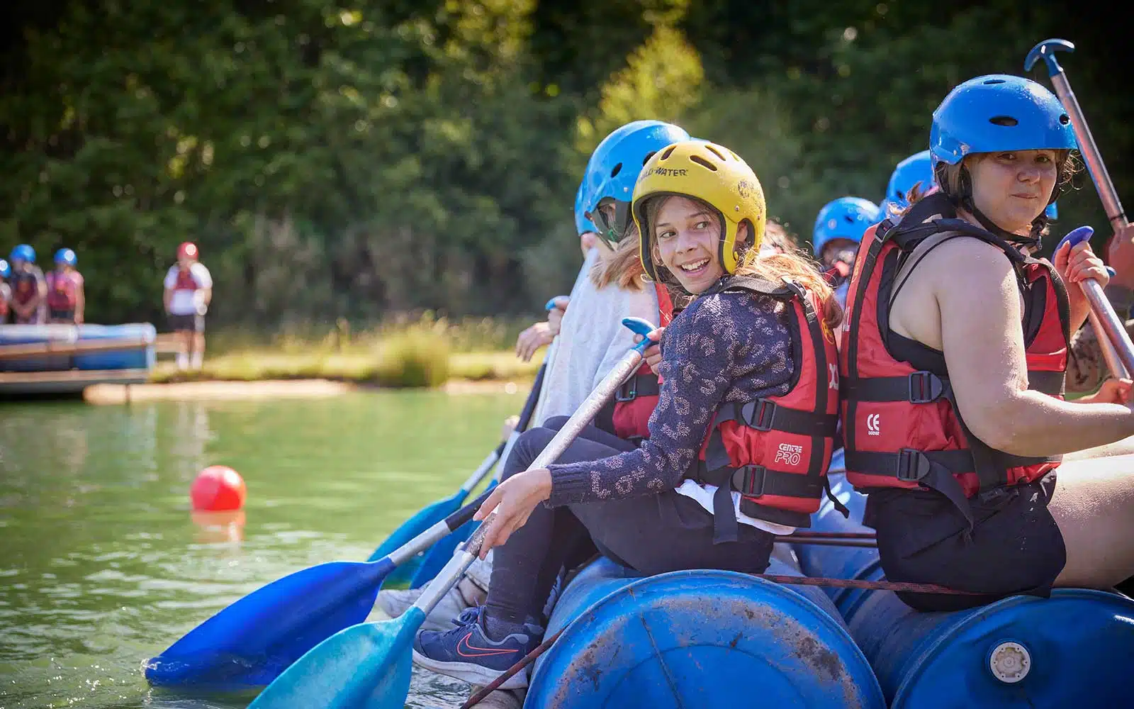 People in helmets and life vests enjoying a rafting adventure on a sunny day.