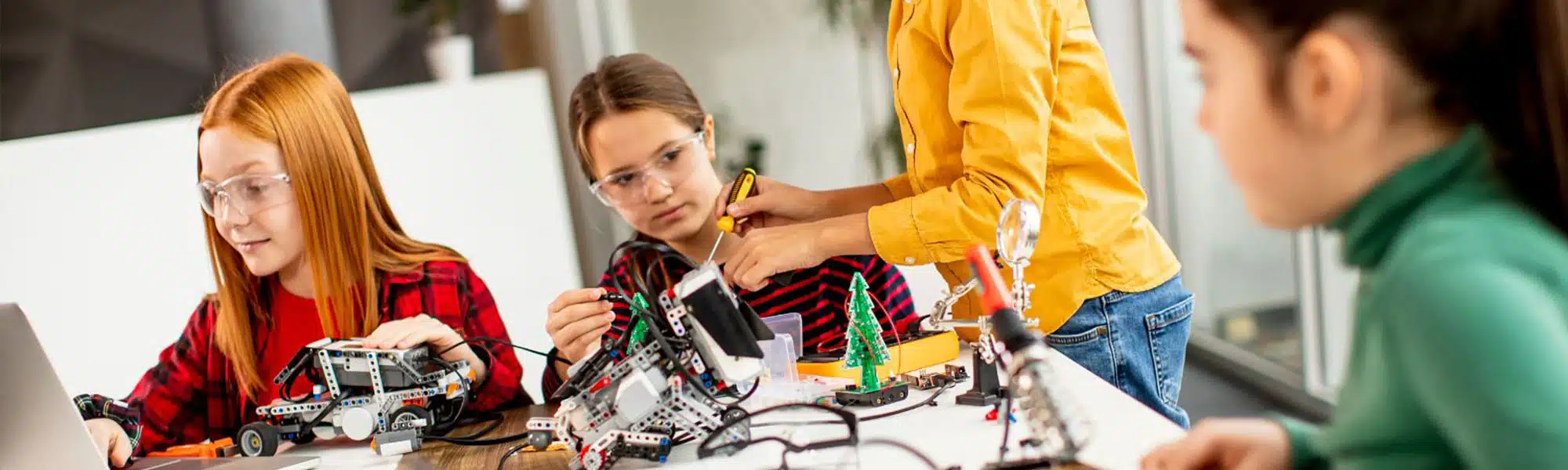 Children engaged in a robotics workshop, building and programming robots at a table with laptops and electronic components.