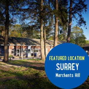 A brick building surrounded by tall trees and grass at Marchants Hill in Surrey, with a blue circle highlighting "Featured Location: Surrey, Marchants Hill.