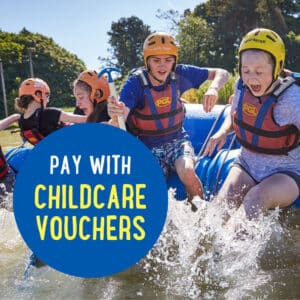 Children wearing life vests and helmets are enjoying a water activity. A blue circle on the image contains the text, "Pay with Childcare Vouchers.