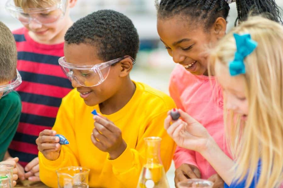 Diverse group of children wearing safety goggles and conducting experiments with small lab equipment at a PGL Adventure Holidays science class.