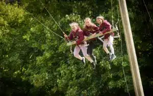 Three young people enjoying a ride on a zip line swing amidst lush green trees.