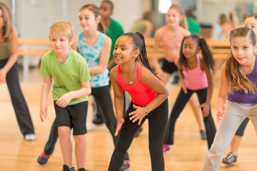 A group of diverse children participating enthusiastically in a PGL Adventure Holidays dance class inside a brightly lit studio.
