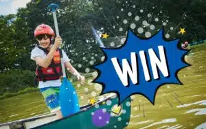 A child wearing a helmet and life jacket paddles a canoe on a lake, with a large 