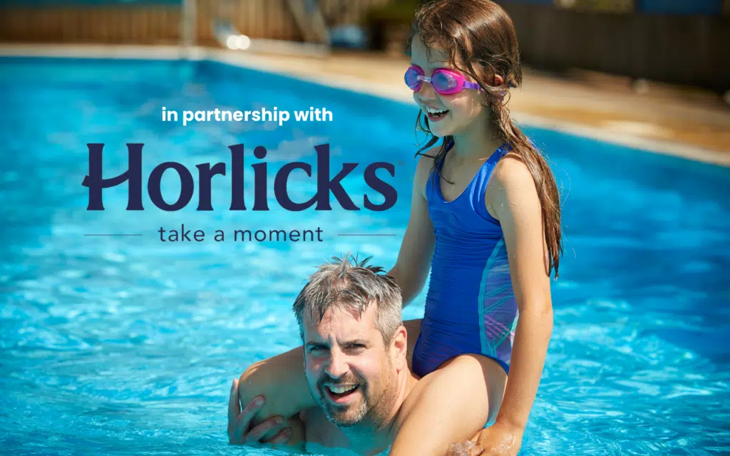 A man with gray hair and a girl in pink goggles and a blue swimsuit are playing in an outdoor pool. The text reads, 