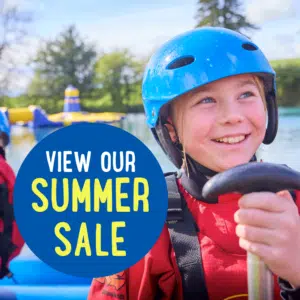 A child wearing a blue helmet and red life vest smiles while holding a handle. Text reads "View Our Summer Sale" against a blue circle background.
