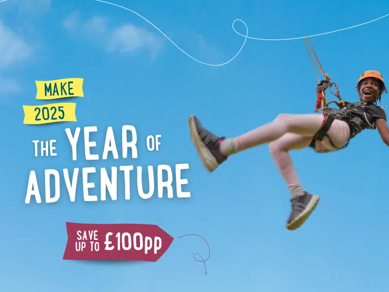 Person ziplining with a wide smile against a clear blue sky. Text reads, 