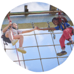 Two individuals in climbing gear touch hands while suspended on a ropes course against a blue sky.