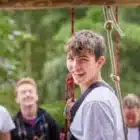 A young person at Learner Driver, Liddington (Aug 10, 2024) smiles at the camera in a harness, while three others stand and laugh outdoors in the background.