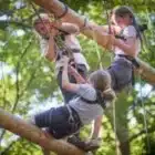 Three children in harnesses and helmets balance on suspended wooden beams at Boreatton Park's Pony Camp Beginner, Jul 20, 2024.