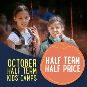 Two children wearing harnesses at an outdoor camp with text promoting October half term kids' camps at half price.