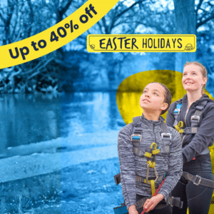 Two girls wearing harnesses outside by water, smiling and looking up. Banner reads "Up to 40% off" and "Easter Holidays" in yellow and blue.