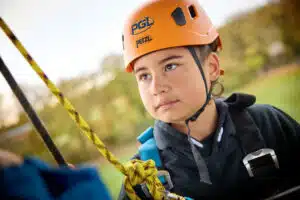 A child wearing an orange helmet and harness looks focused whilst participating in an outdoor climbing activity during their PGL Adventure Holidays.