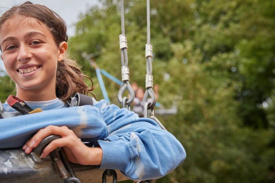 The child at the forefront is smiling at the camera while suspended during a climbing activity at a PGL kids camp