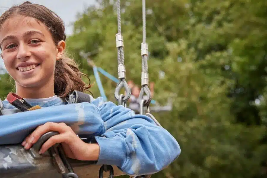 The child at the forefront is smiling at the camera while suspended during a climbing activity at a PGL kids camp