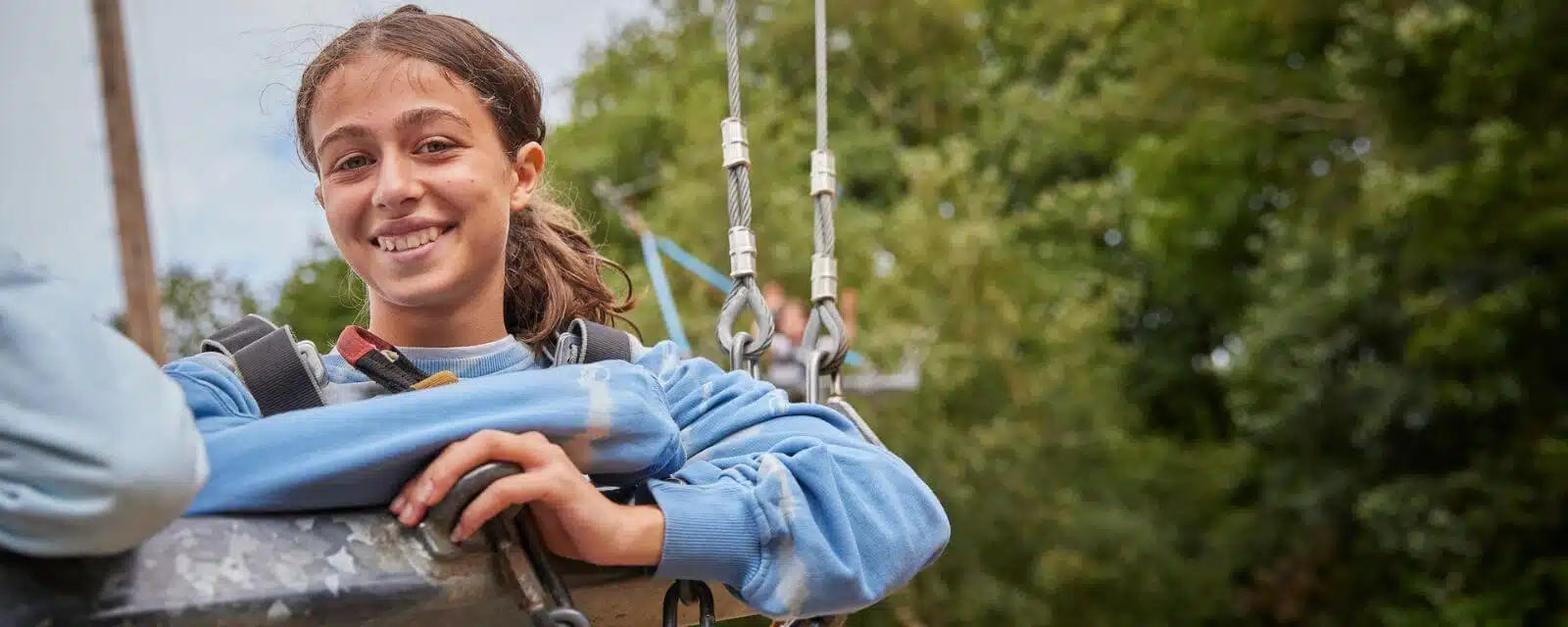 The child at the forefront is smiling at the camera while suspended during a climbing activity at a PGL kids camp