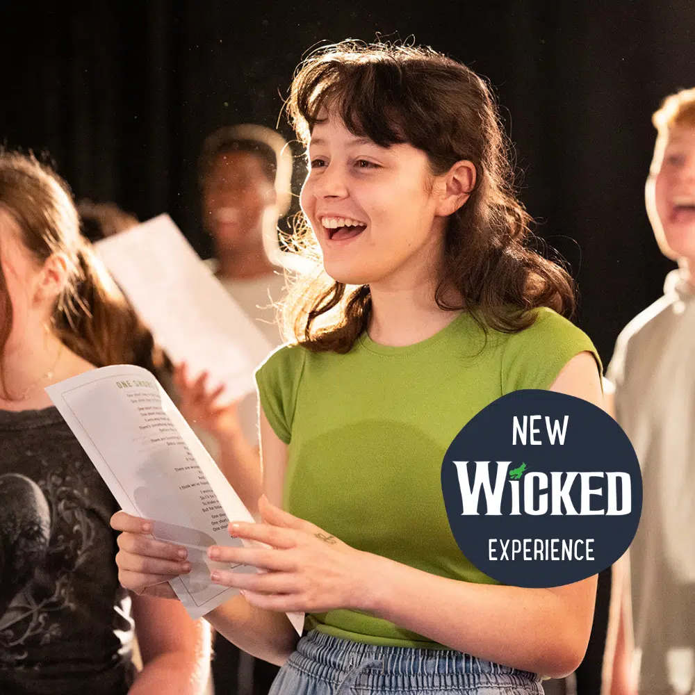 A young person in a green shirt holds sheet music and sings with a group during PGL Adventure Holidays. A 