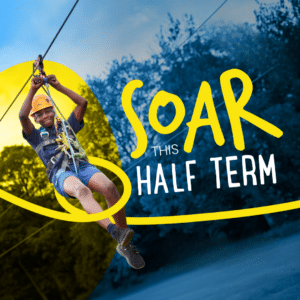 A child wearing a helmet and harness rides a zip wire outdoors, with bold text reading “SOAR THIS HALF-TERM” overlaid on the image.