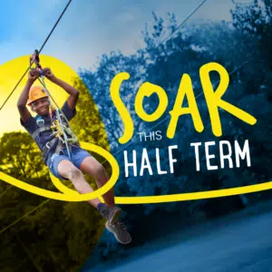 A child wearing a helmet and harness rides a zip wire outdoors, with bold text reading “SOAR THIS HALF-TERM” overlaid on the image.