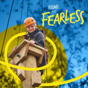 Smiling child in a helmet and harness climbs a wooden pole outdoors, with text reading “Found My Fearless” over a blue and yellow background.