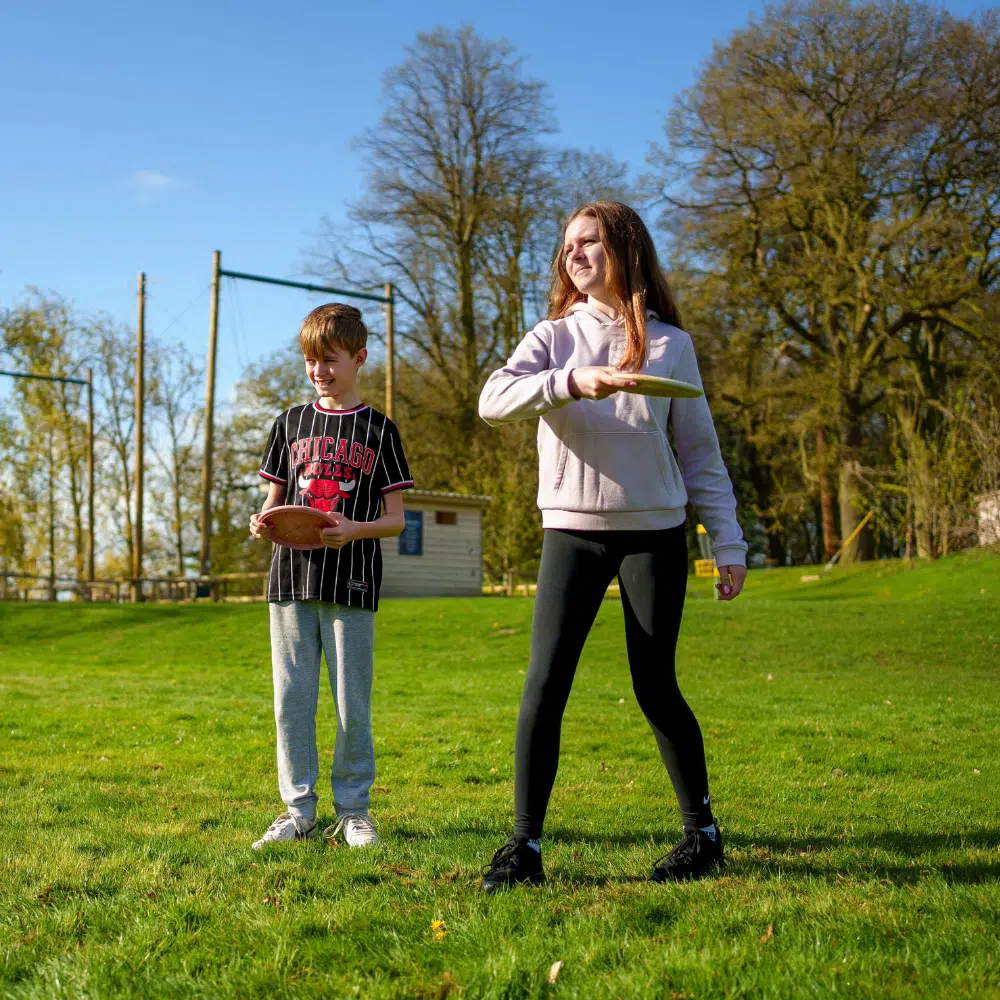 A boy and a girl standing on a grassy field, each holding a disc.