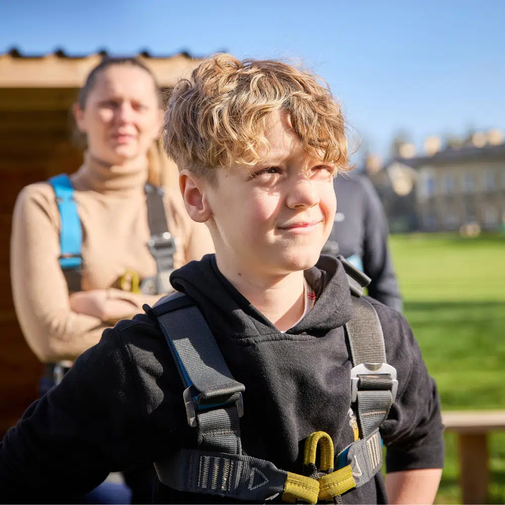 A young person in a climbing harness with an adult standing in the background.